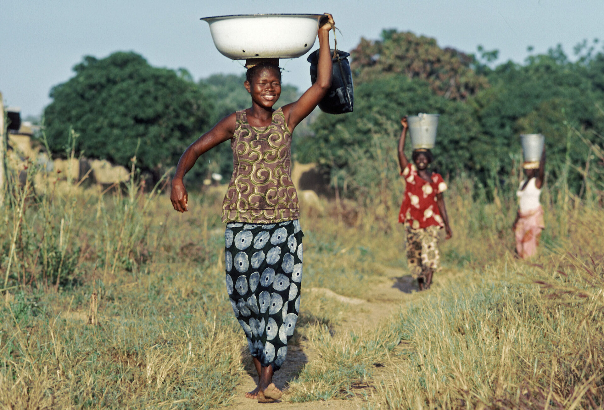 village women carry containers full of water from the well
