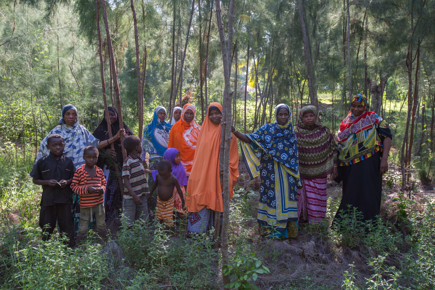 Women and children standing beneath trees they planted in community forest