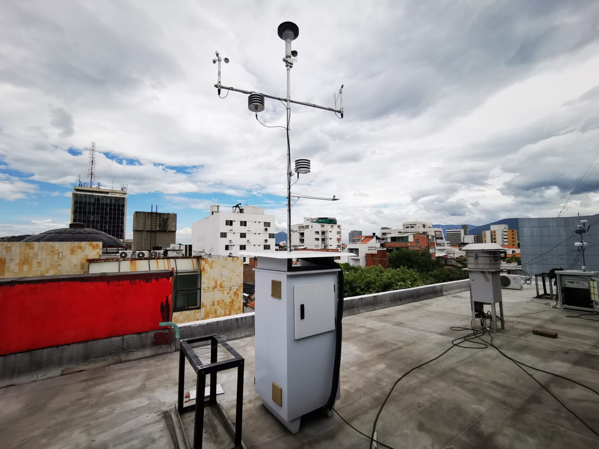 a white weather monitoring station on a roof against a background of residential mid-rise buildings