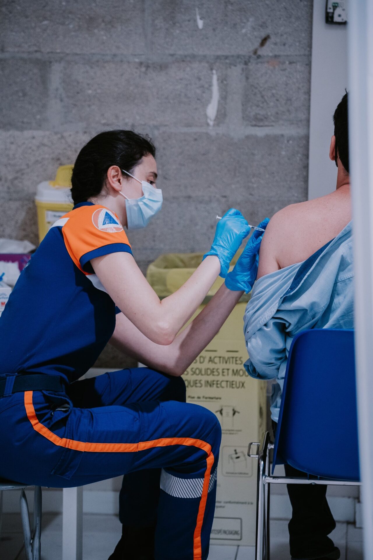 a woman in a blue and orange uniform give a vaccine to a man