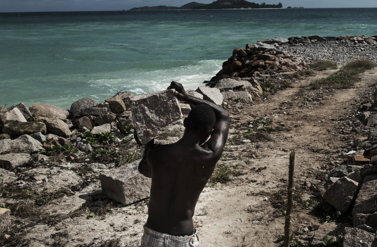 A man carrying a rock towards the coast to build protective barriers