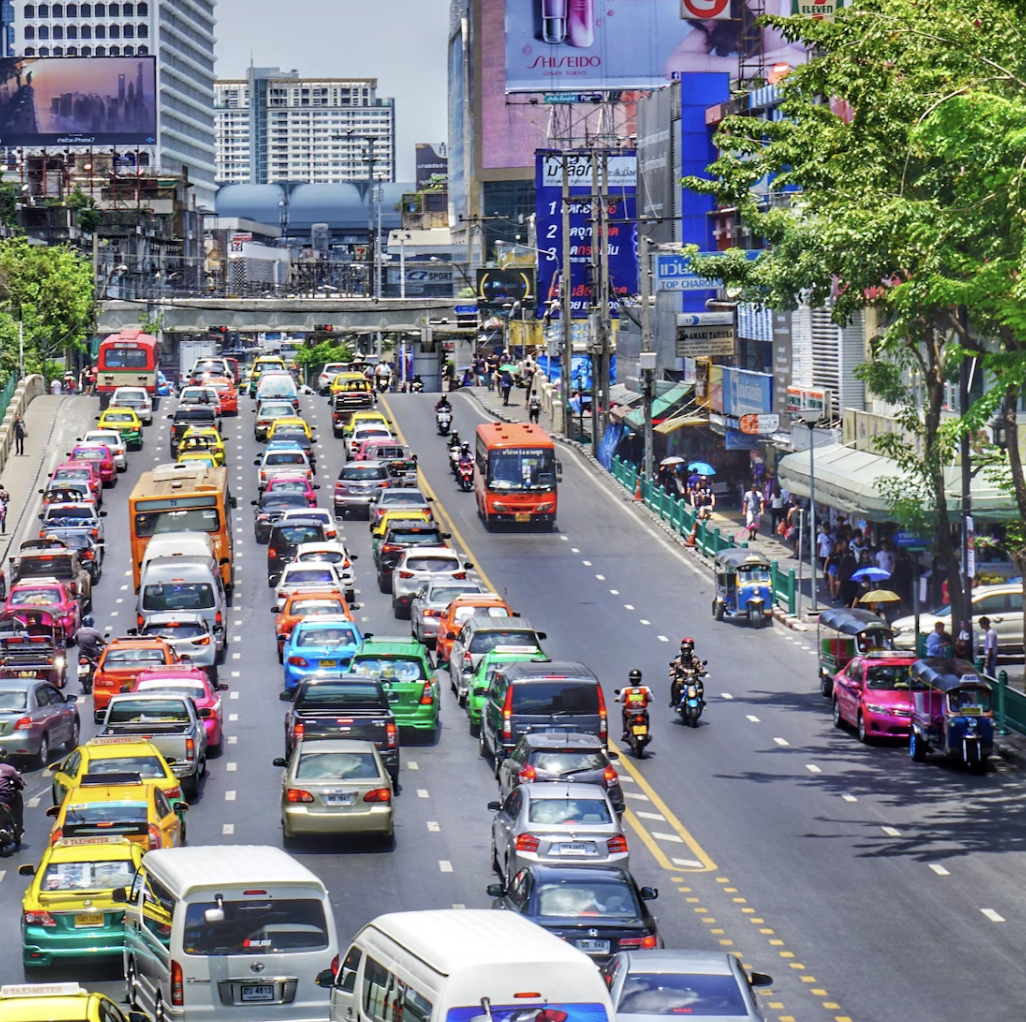 Traffic in Bangkok on a road surrounded by tall buildings and trees