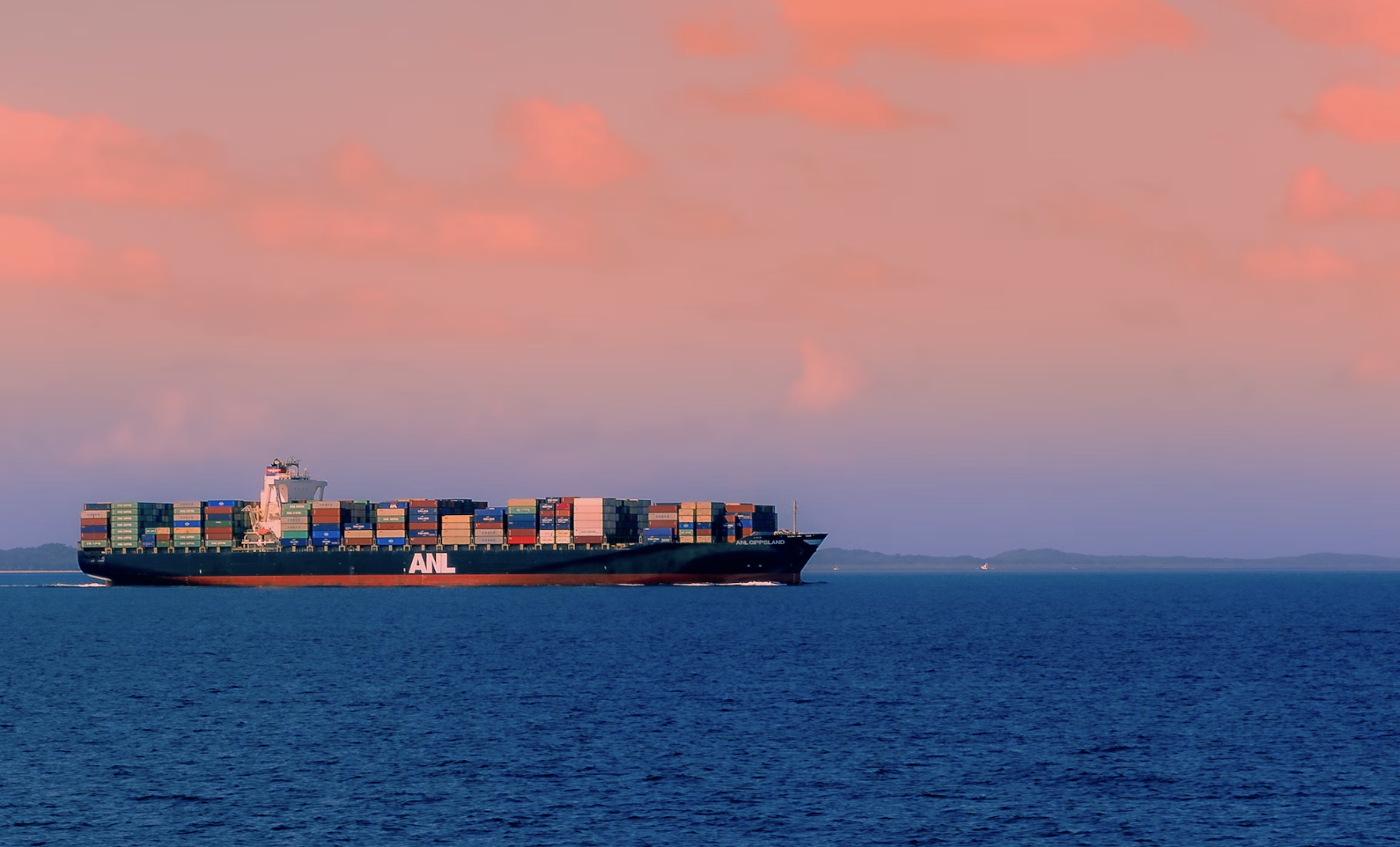 Container ship separated by blue sea and pink sky