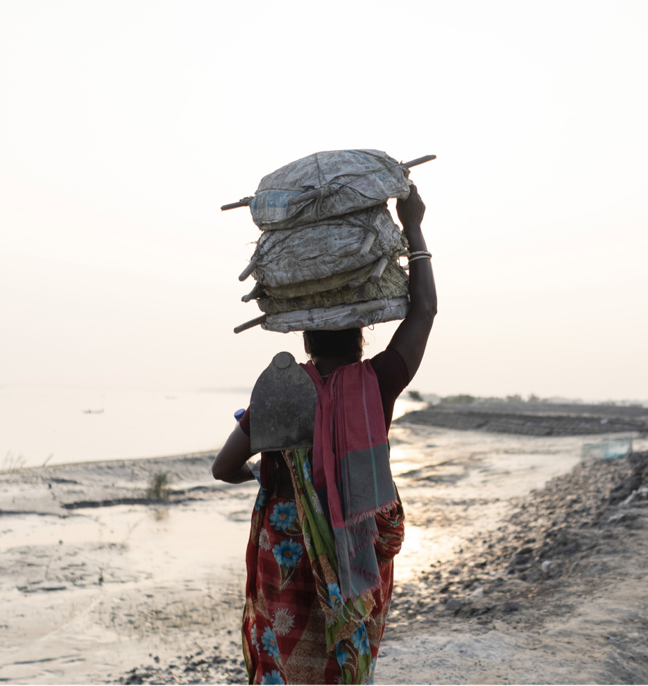Woman on her way to repaid a damaged embankment in Munshiganj, Shyamnagar, carrying supplies on her head