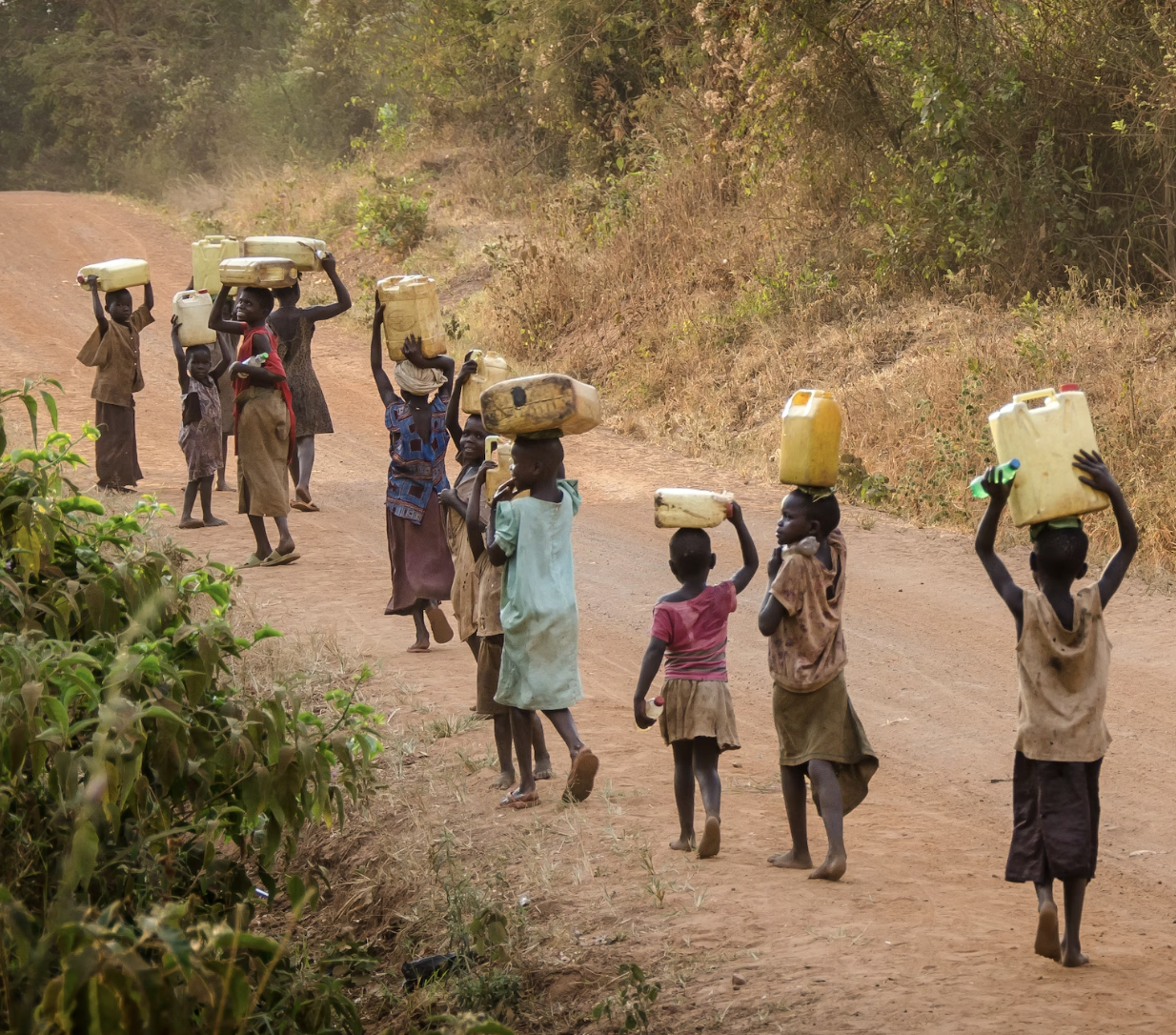 A group of children walking down a road carrying containers on their heads