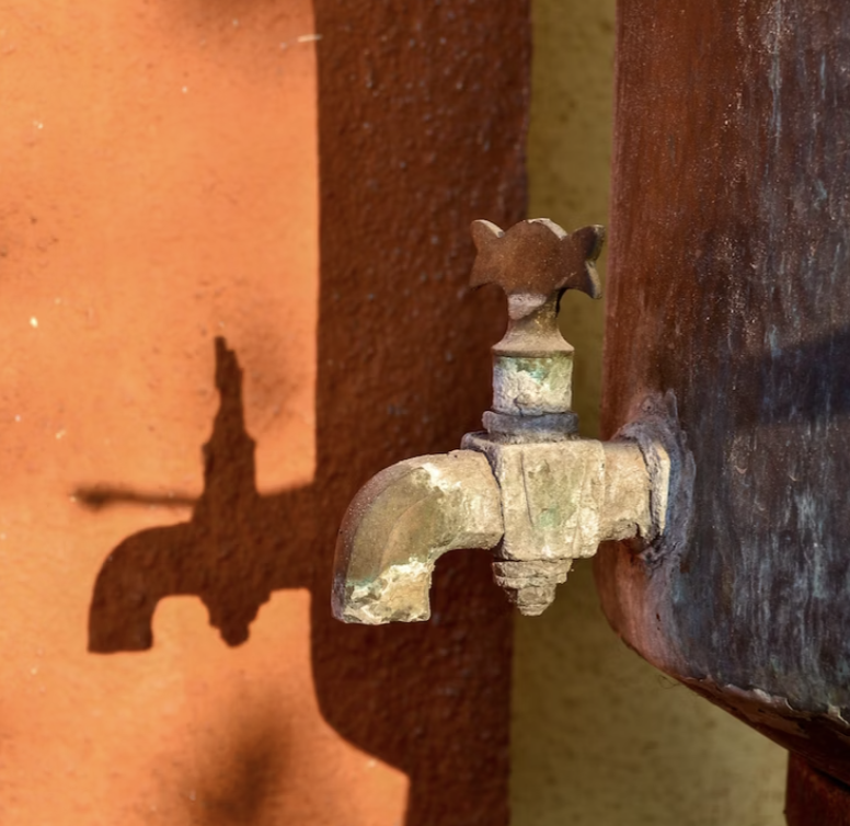 A water tap on a clay-colored wall