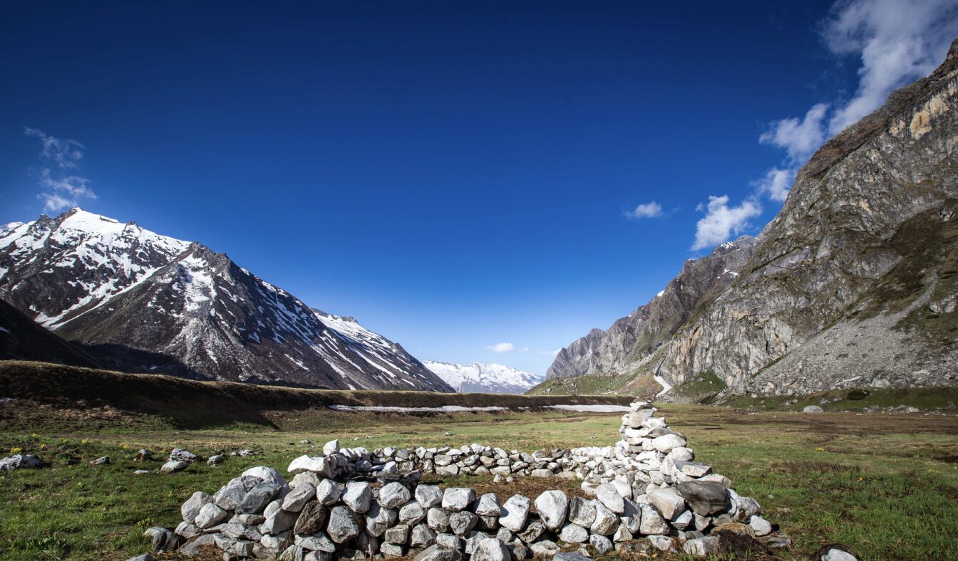 blue sky with grey mountains, green grass and a circle of rocks