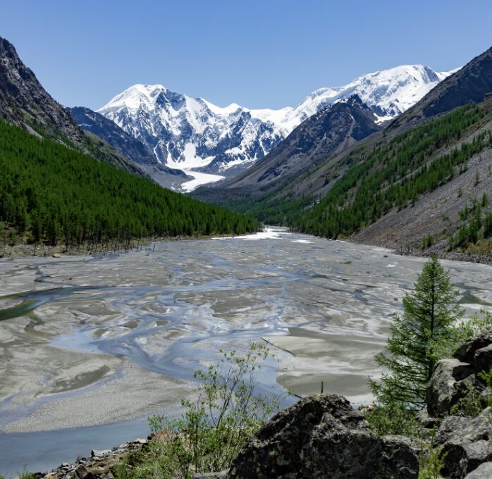 A river running through a valley surrounded by mountains with snow and green trees
